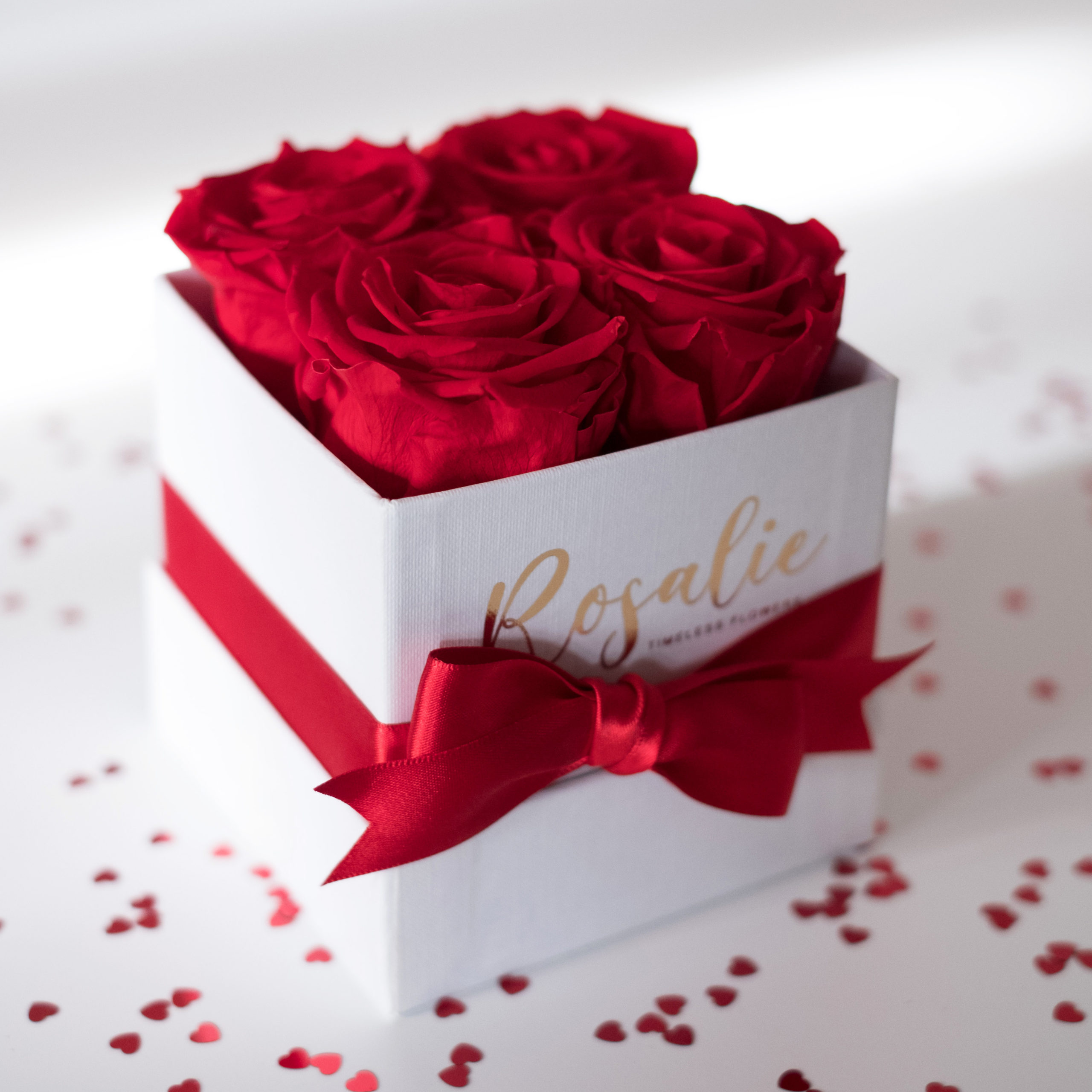 scatola box quadrata con 4 rose rosse stabilizzate e fiocco rosso su tavolo bianco