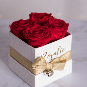 scatola bianca quadrata con 4 rose stabilizzate rosse e nastro dorato su tavolo bianco