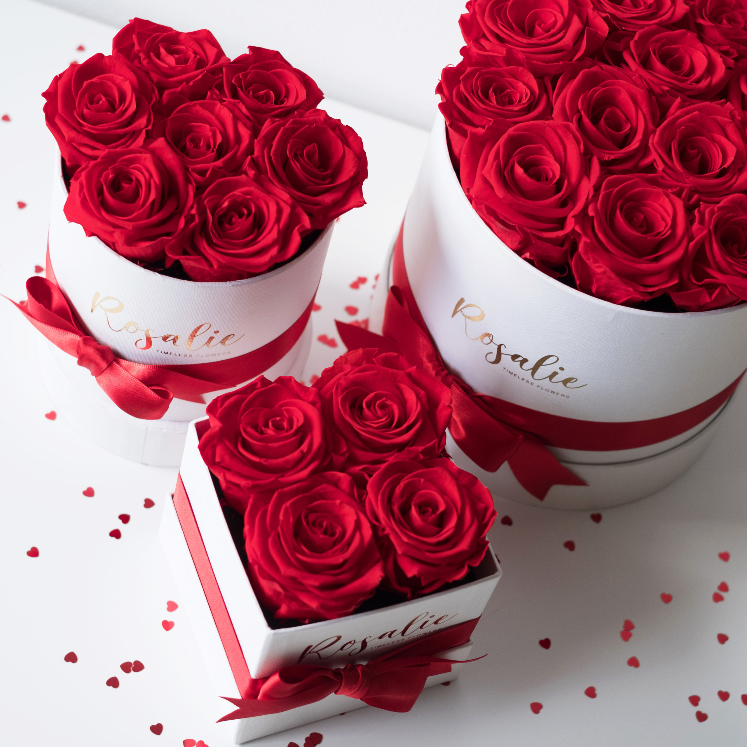 tre scatole con rose rosse stabilizzate viste dall'alto su tavolo bianco
