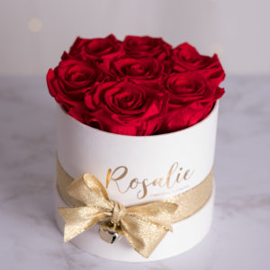 scatola tonda bianca con 7 rose stabilizzate di color rosso con fiocco oro su tavolo di marmo bianco