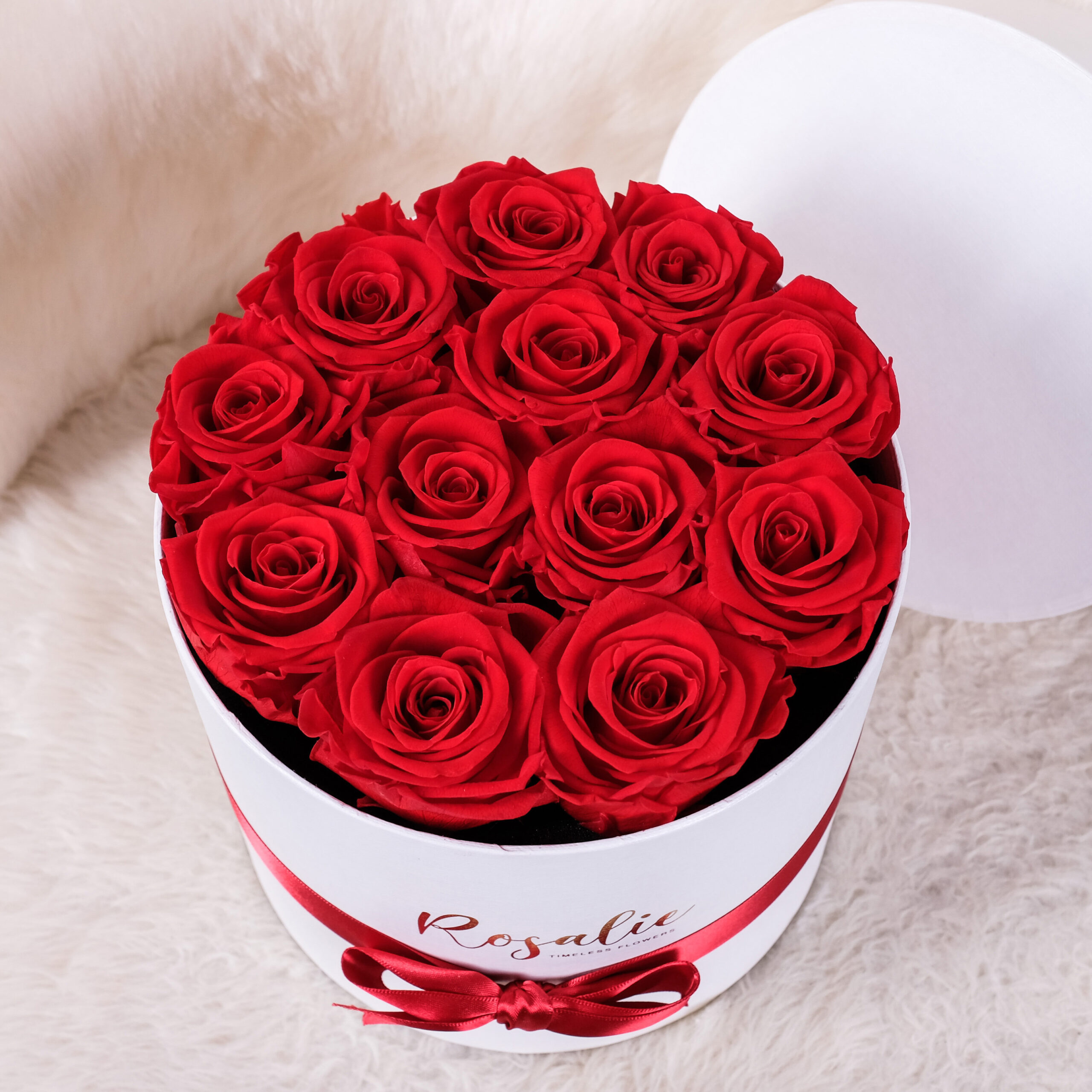 box tondo con 12 rose rosse stabilizzate su sedia bianca