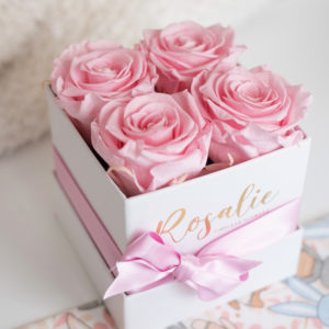 quattro rose stabilizzate di color rosa in scatola quadrata con nastro rosa con fiocco, visto dall'alto. Su tavolo bianco.