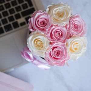 scatola con 7 rose stabilizzate in scatola tonda sopra computer su tavolo bianco