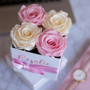 scatola quadrata con 4 rose stabilizzate di cui due di color rosa e due panna accanto a orologio