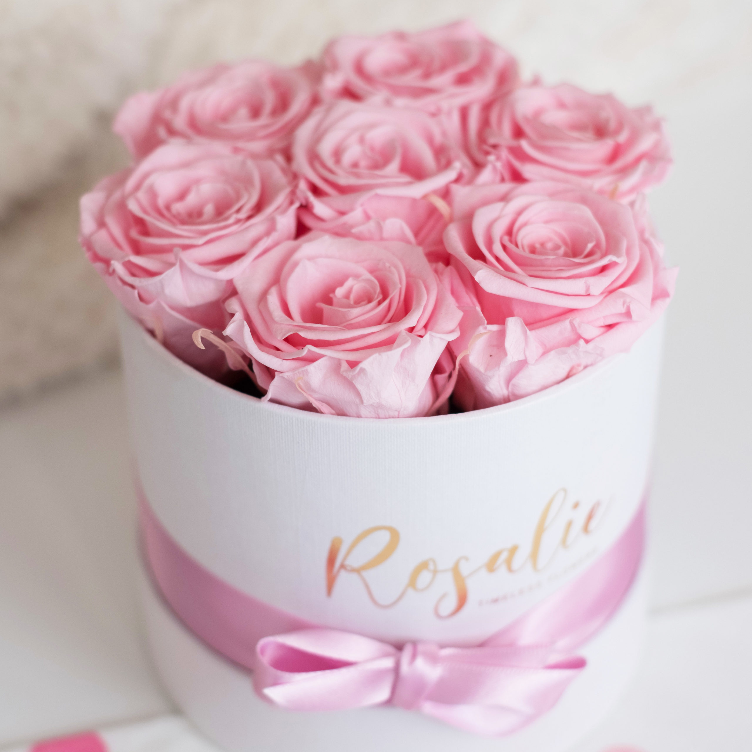 box con 7 rose stabilizzate di color rosa e nastro rosa. Su tavolo bianco. Visto dall'alto.