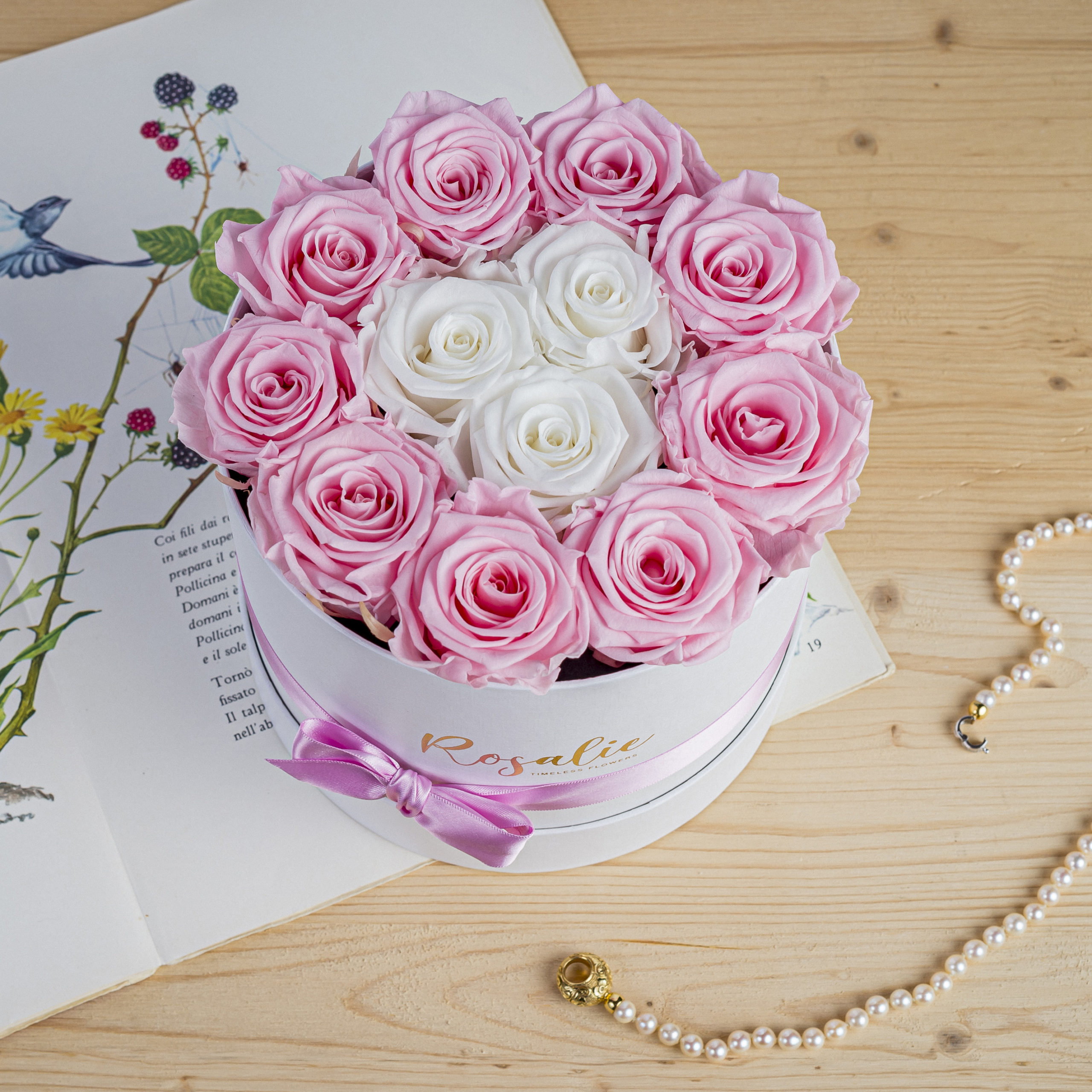 Elegante scatola tonda con 12 rose stabilizzate appoggiata su un tavolo di legno vicino a un libro di fiabe