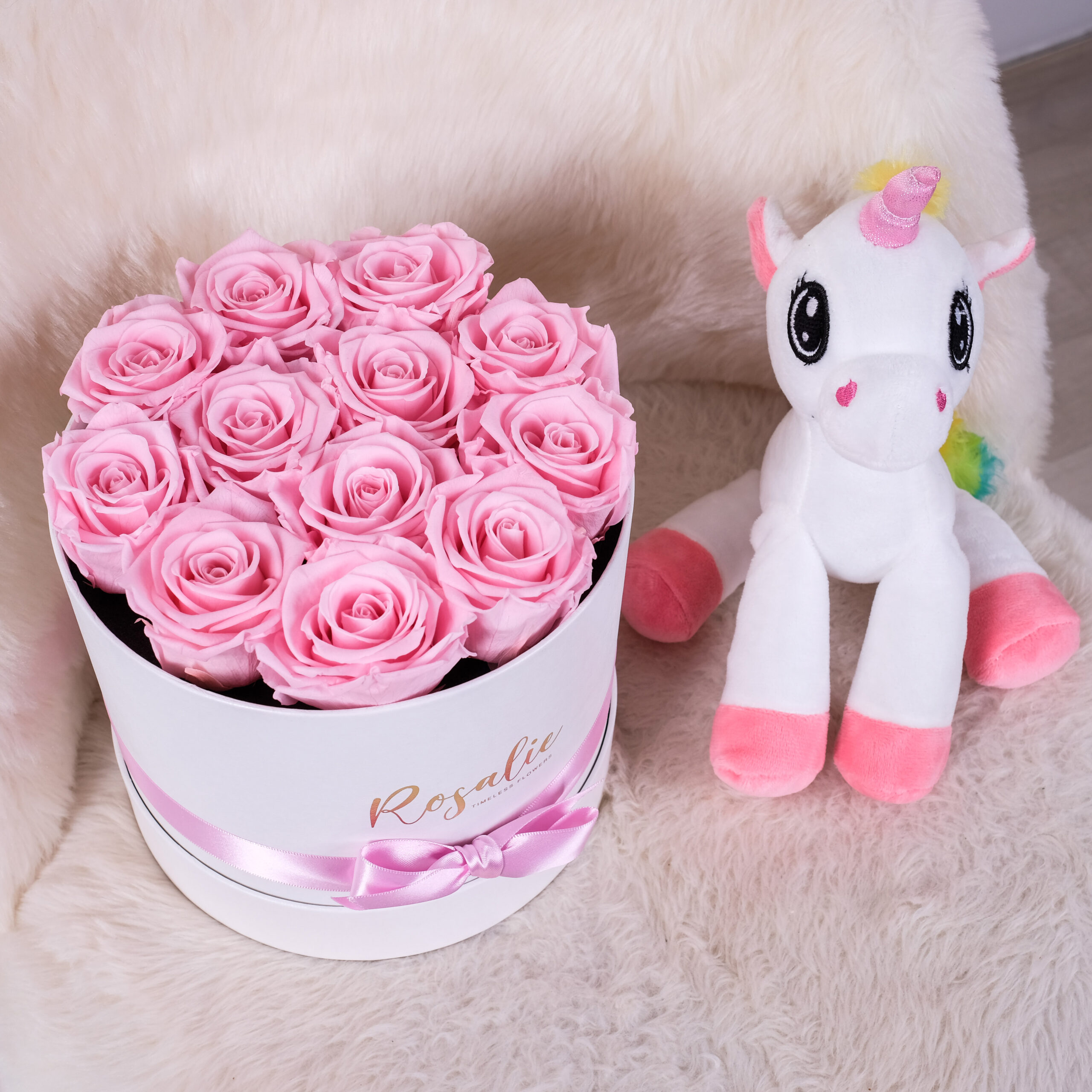 scatola tonda con 12 rose stabilizzate di color rosa accanto a pupazzo a forma di unicorno