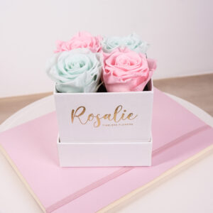 scatola quadrata con 4 rose stabilizzate di color rosa e verde menta su quaderno rosa e tavolo bianco