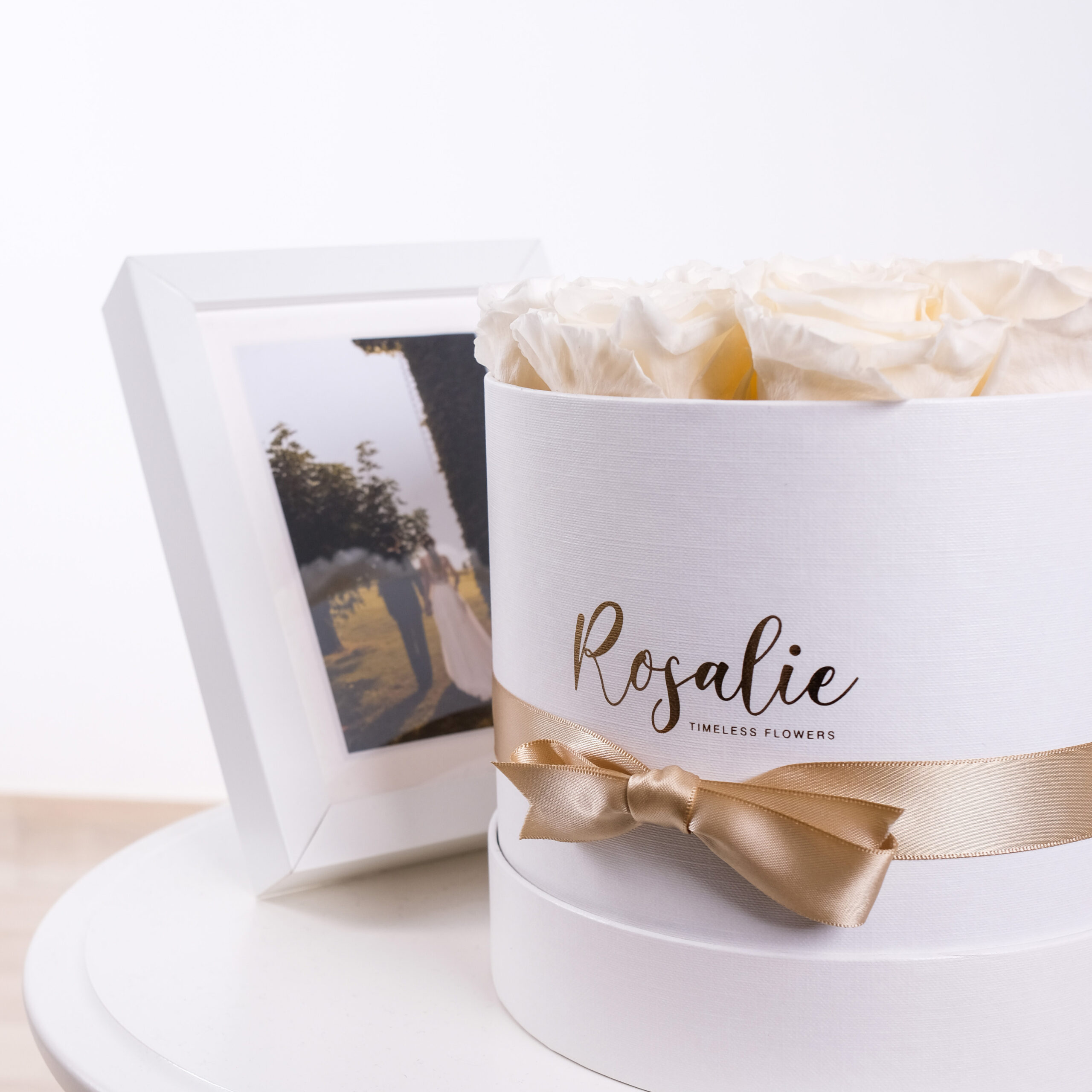 box tondo con rose stabilizzate color bianco panna e nastro dorato con accanto cornice con sposi