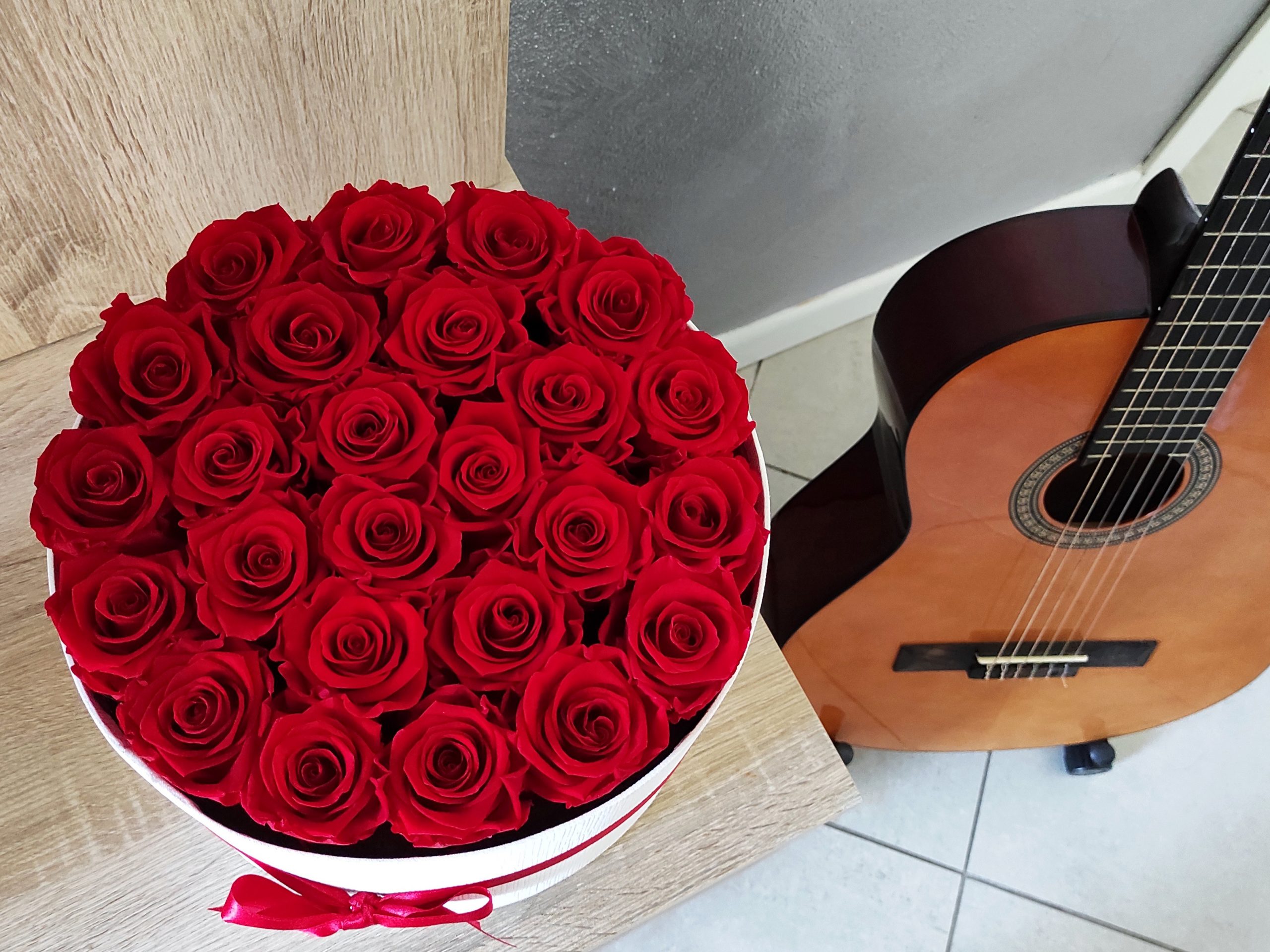 scatola di rose stabilizzate tonda con 25 rose rosse accanto a chitarra