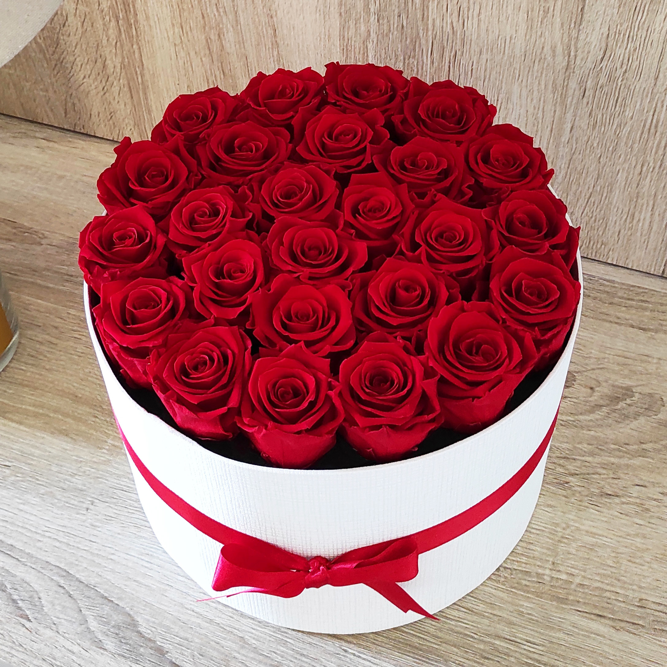 scatola bianca tonda con 25 rose rose stabilizzate e nastro rosso abbinato