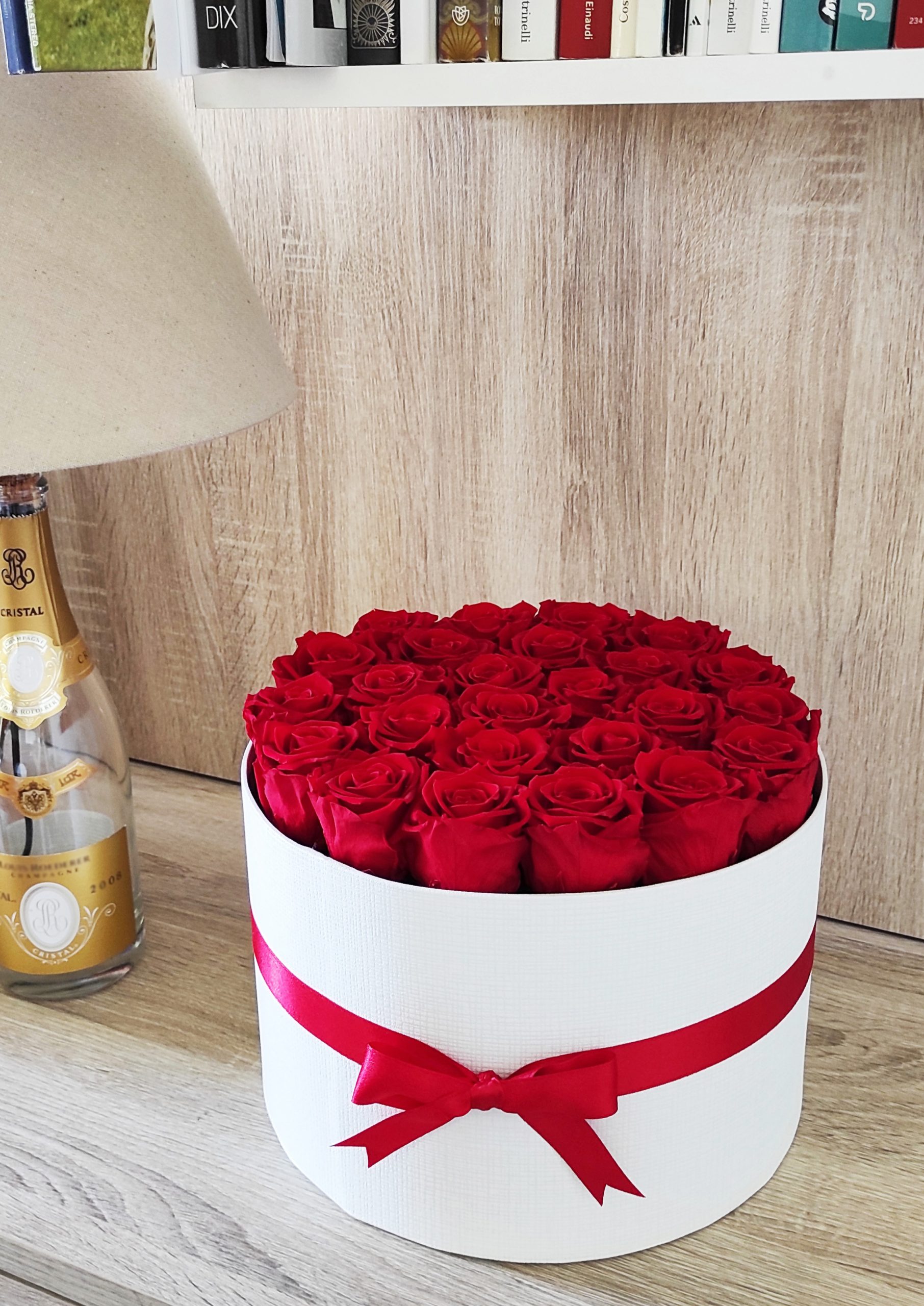 box con 25 rose stabilizzate rosse vicino a lampada bottiglia su ripiano di legno